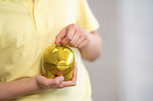 A close-up shot of a person's hands carefully placing coins into a piggy bank, symbolizing the act of saving for retirement. The background is blurred to focus on the hands and the coins.