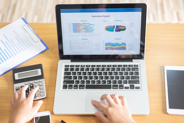 A detailed budget spreadsheet displayed on a laptop, showing income, expenses, and savings categories, with a person using a calculator to analyze the data.