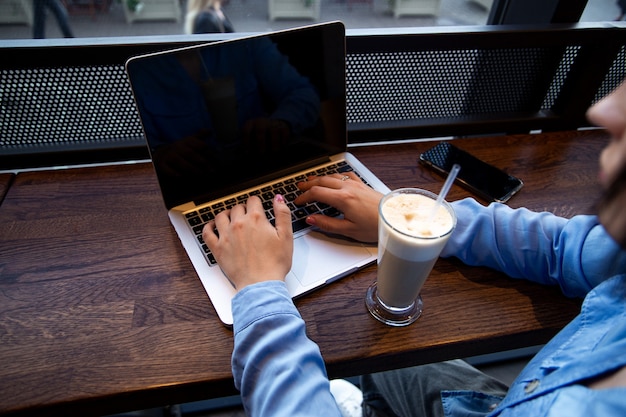A person working on a laptop at a coffee shop, with a notebook and pen beside them, symbolizing freelancing or a side hustle for extra income.