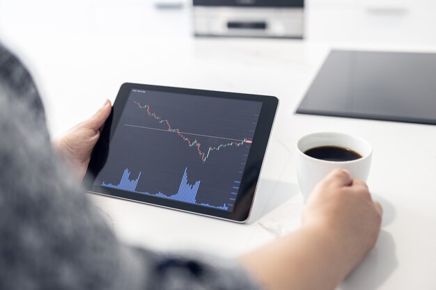 A person looking at a graph on a tablet showing an upward trend in interest rates, overlaid with dollar signs. The setting is a modern, minimalist home office.