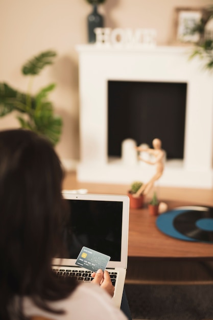 A person using a laptop to manage their credit card accounts and make online payments. The scene is set in a home office with financial charts and graphs visible in the background.