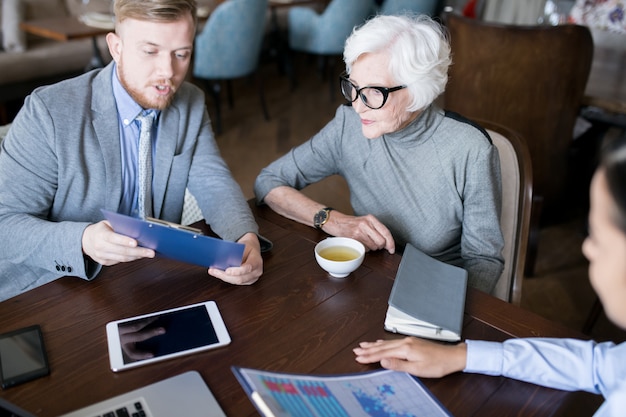 A financial advisor meeting with a client, discussing retirement plans and Social Security benefits using charts and graphs. The setting is a modern office with a collaborative atmosphere.