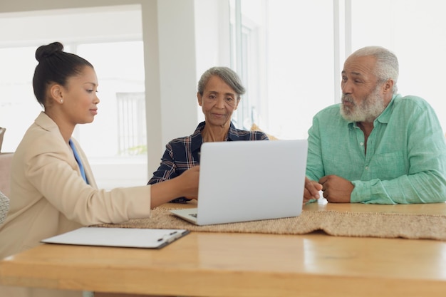 An insurance agent discussing long-term disability insurance options with a client at a conference table. They are looking at policy documents and a laptop displaying insurance plans.