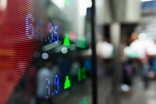 A close-up of a digital display showing inflation rates and unemployment percentages. The screen is set against a blurred background of a bustling financial trading floor.