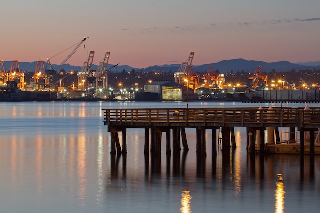 A cargo ship docks at the port of Los Angeles, California, containers of goods being loaded. The sun is setting and the containers are being loaded or unloaded.