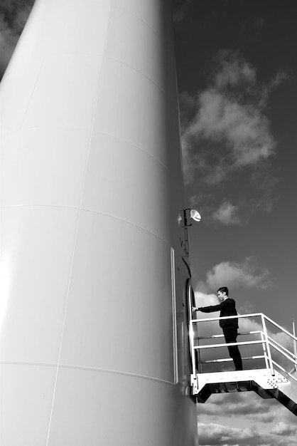 A detailed close-up of a technician inspecting a modern wind turbine blade, highlighting the advanced materials and engineering involved in its construction. The backdrop shows a wind farm against a sunset, illustrating the blend of technology and nature.