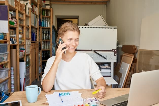 A person smiling confidently while talking on the phone, sitting in a well-organized home office. The background includes bookshelves and a computer monitor, suggesting a productive environment.
