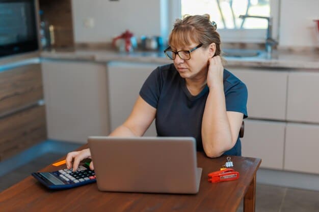 A close-up of an employee looking stressed while reviewing their household budget on a laptop, with bills and receipts scattered around. A calculator is visible, highlighting the financial strain caused by rising inflation.