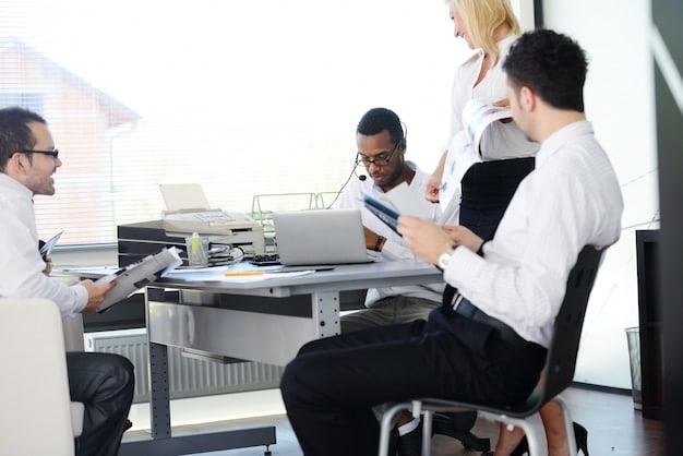 A diverse group of employees collaborating in a modern office space, with laptops and documents spread across a table. The image depicts a positive and productive work environment, emphasizing diversity and teamwork.