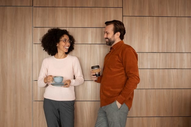 Two colleagues are chatting in a relaxed office corner. One of them is holding a baby photo, triggering a heartwarming and supportive conversation. The scene represents workplace empathy and family-friendly environment.